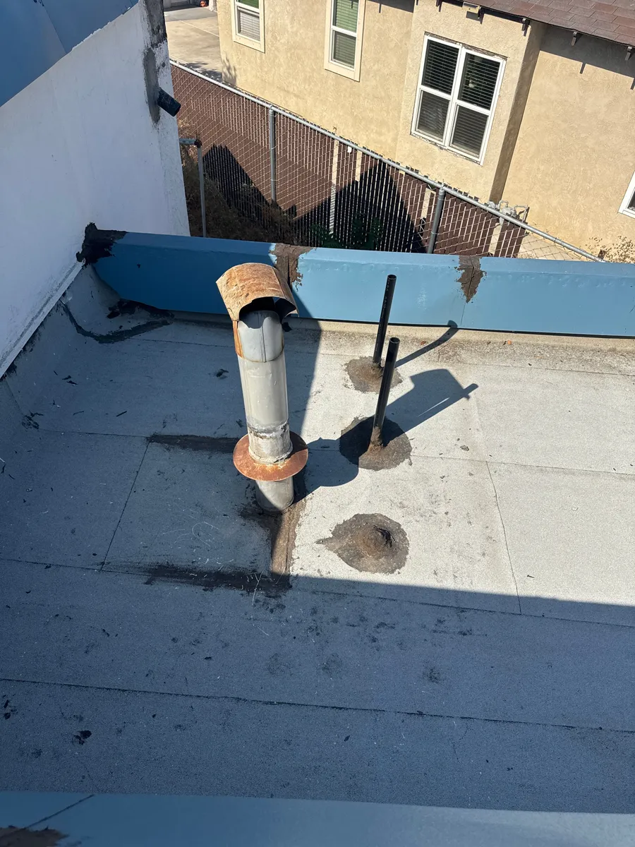 Weathered flat roof with a rusted vent pipe and failing penetration flashing at Beto's Bakery before coating