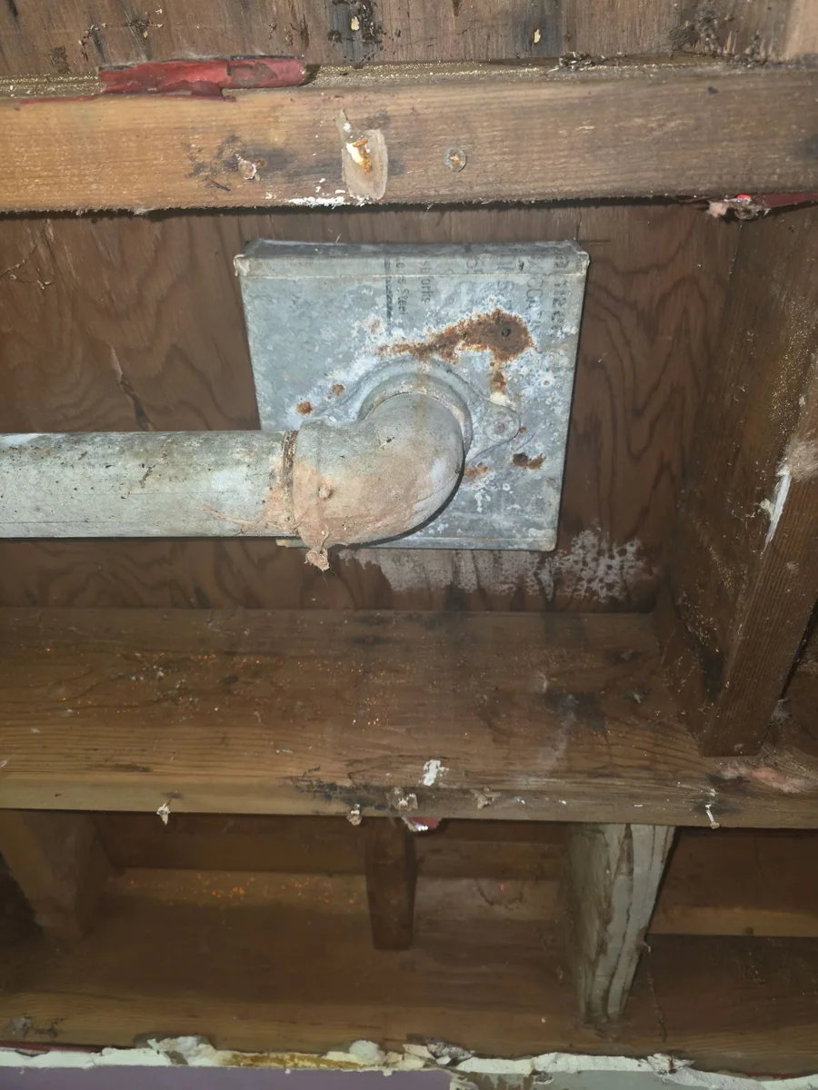 Corroded roof-drain assembly and water-stained framing inside the ceiling cavity beneath the failed Modesto drain