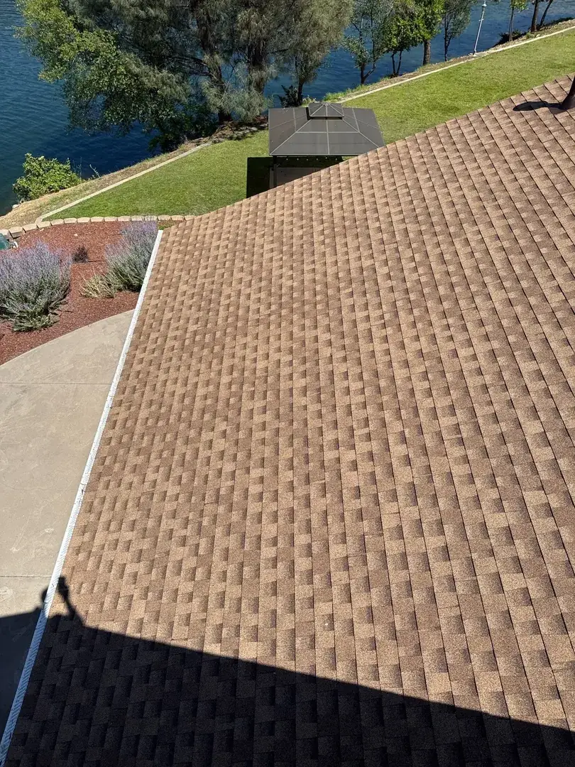 New brown architectural shingles and a clean gutter line above the landscaped yard and gazebo at the Jamestown lakefront home