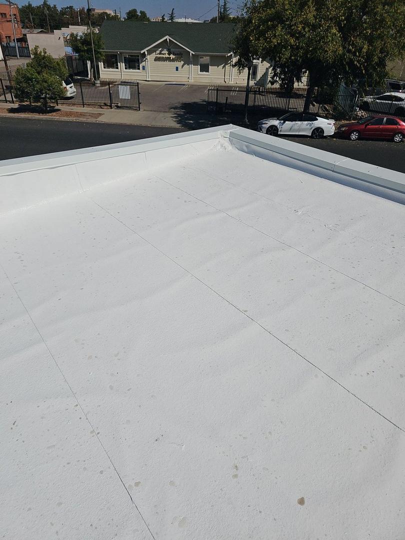 Completed white elastomeric coating with clean metal edge and Modesto street view