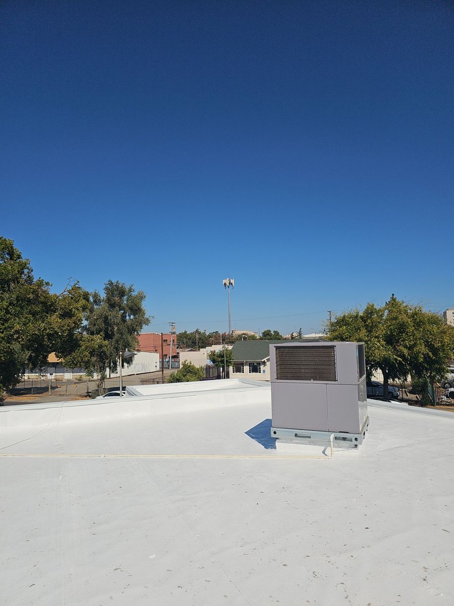 HVAC unit on pristine white coated commercial roof against blue sky