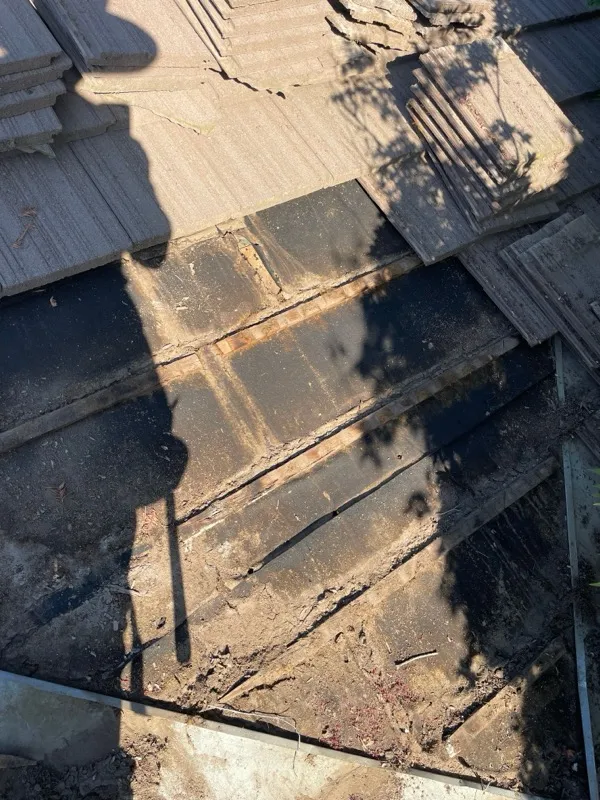 Concrete tiles removed and stacked, exposing weathered felt underlayment, during the Riverbank tile roof repair