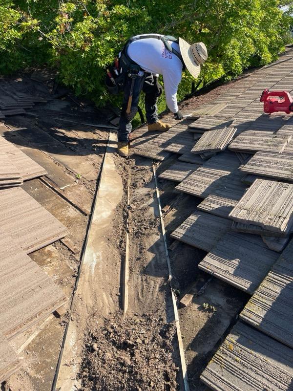 Worker removing damaged tiles along roof valley